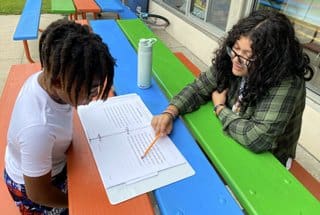 Two people sitting at a table with papers and pencils.