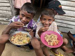 Two children eating food from a plate.