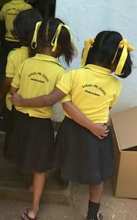 Two young girls in yellow shirts and black skirts.