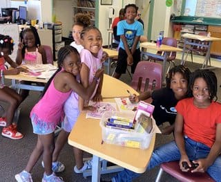 A group of children sitting at tables in a classroom.