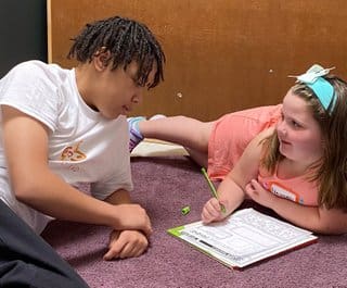 Two people are laying on the floor and one is writing.