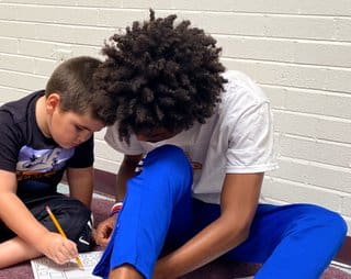 A boy and his friend are writing on paper.