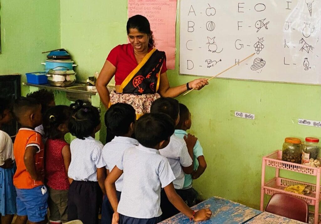 A woman teaching children in front of a whiteboard.